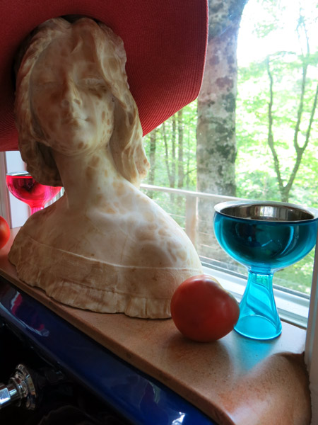 curved concrete windowsill with bust statue of woman, tomato and blue glass