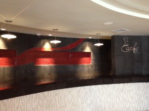 long curved black concrete countertop in bar with red glass tile
