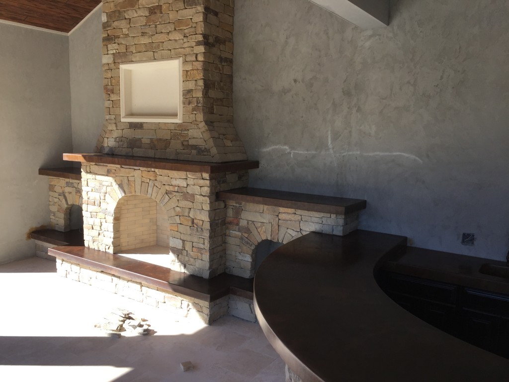 outdoor kitchen with brown curved concrete countertop and stacked stone fireplace