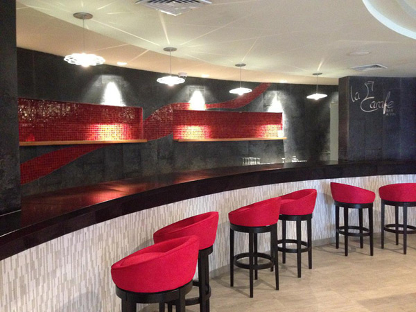 long curved black concrete countertop in bar with red glass tile and red barstools